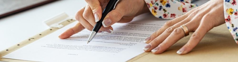 Two hands, one holding a pen, scanning across a piece of paper on a desktop.