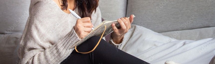 woman, siting on pillow in front of her couch, writing.